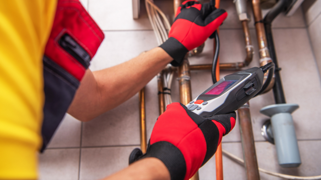 close up of a person with red gloves testing electrical equipment with a handheld device.